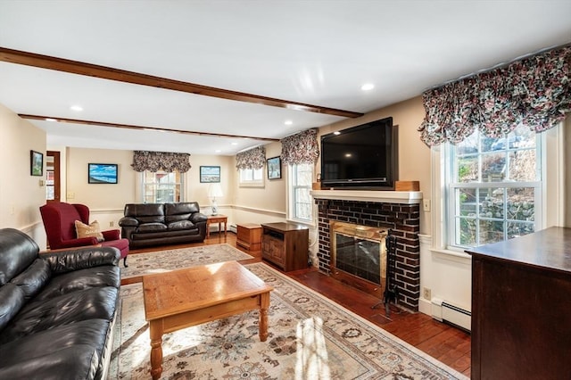 living room with a baseboard heating unit, dark wood-type flooring, a brick fireplace, and a healthy amount of sunlight