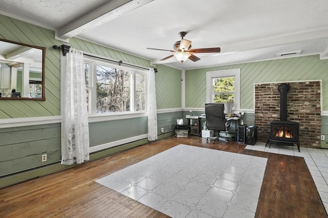 office area featuring a wood stove, a healthy amount of sunlight, beamed ceiling, and wood finished floors