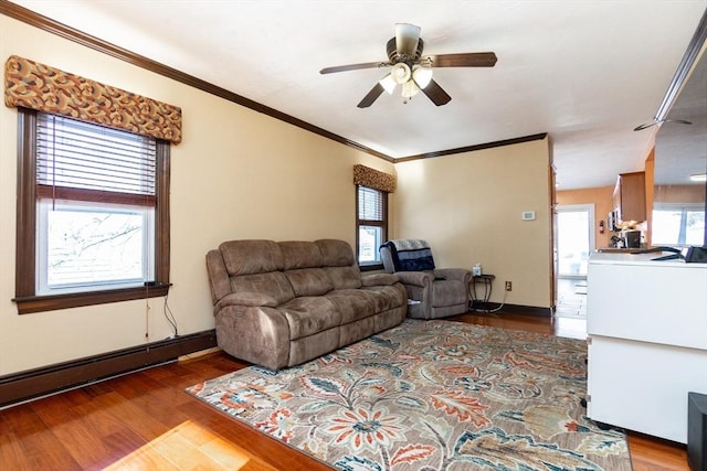 living room featuring baseboard heating, hardwood / wood-style flooring, ceiling fan, and ornamental molding