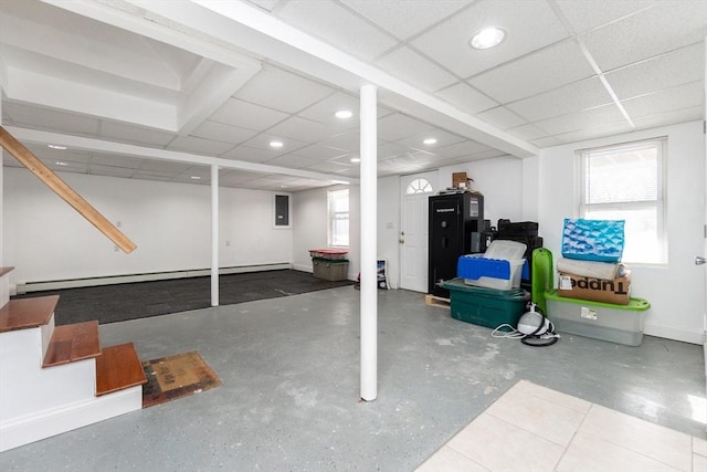 basement with a baseboard radiator, plenty of natural light, and a drop ceiling