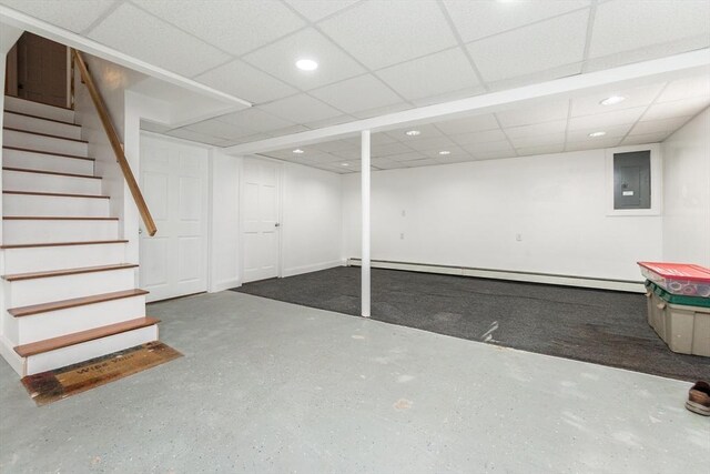 basement featuring a paneled ceiling, electric panel, and a baseboard heating unit