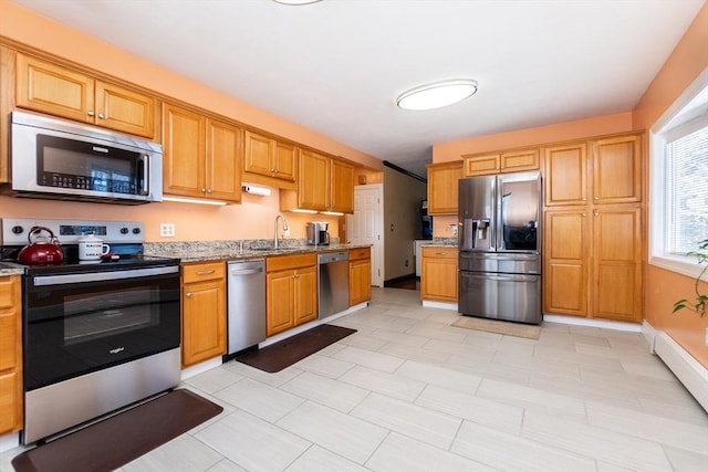 kitchen with light stone counters, baseboard heating, appliances with stainless steel finishes, and sink