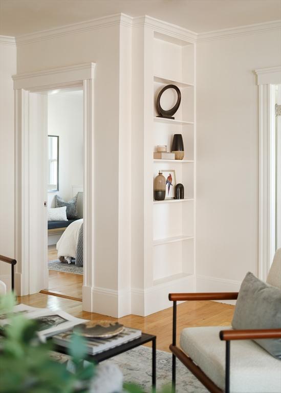 sitting room featuring built in features, baseboards, wood finished floors, and crown molding