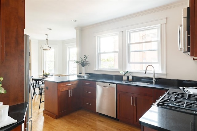 kitchen featuring dark countertops, light wood-type flooring, a peninsula, stainless steel appliances, and a sink