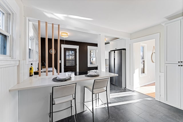 kitchen with white cabinetry, a kitchen bar, kitchen peninsula, dark hardwood / wood-style flooring, and stainless steel refrigerator