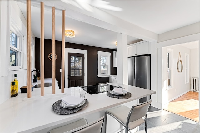 kitchen featuring black electric stovetop, a wealth of natural light, white cabinets, and stainless steel fridge