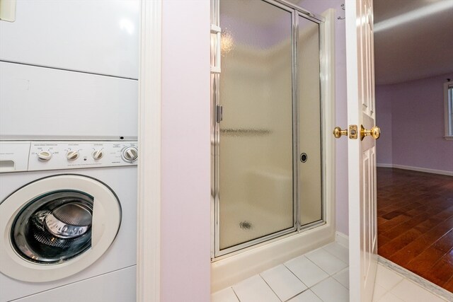 bathroom with a stall shower, tile patterned flooring, baseboards, and stacked washing maching and dryer