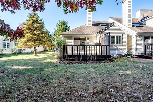 rear view of house with a chimney, a deck, and a lawn