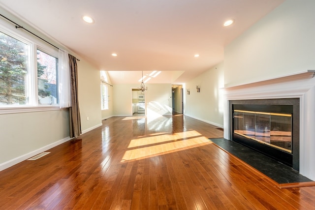 unfurnished living room featuring a glass covered fireplace, visible vents, dark wood finished floors, and baseboards