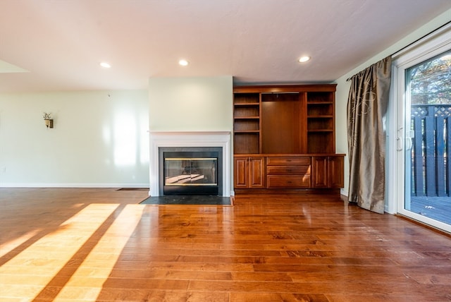 unfurnished living room with a fireplace with flush hearth, baseboards, wood finished floors, and recessed lighting