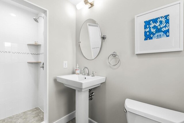 full bath with toilet, tiled shower, a sink, and baseboards