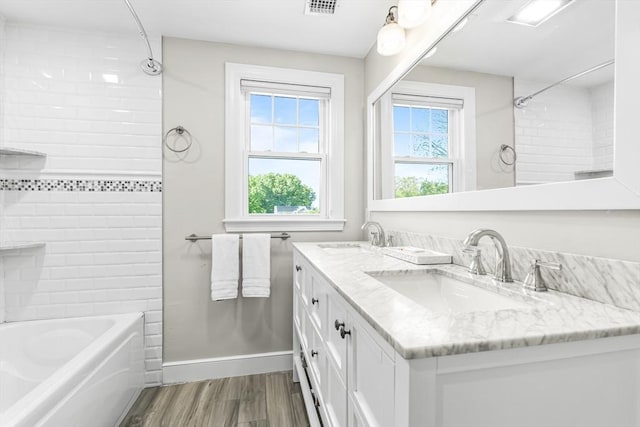 full bath featuring plenty of natural light, wood finished floors, double vanity, and shower / washtub combination