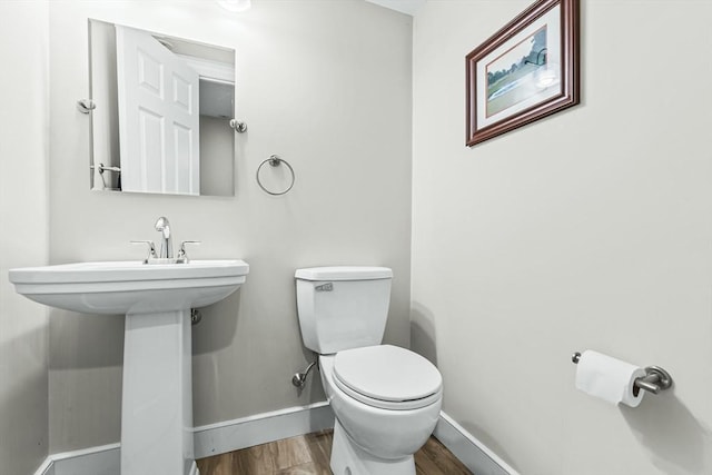 bathroom with baseboards, wood finished floors, toilet, and a sink