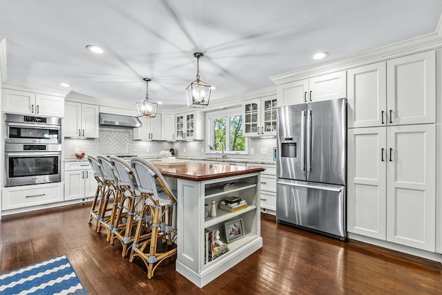 kitchen with appliances with stainless steel finishes, wood counters, wall chimney exhaust hood, white cabinetry, and recessed lighting