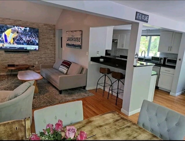 interior space with sink, light hardwood / wood-style flooring, white cabinets, decorative backsplash, and vaulted ceiling