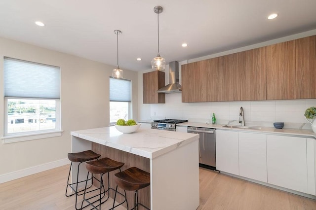 kitchen with wall chimney exhaust hood, a kitchen island, appliances with stainless steel finishes, a kitchen breakfast bar, and a sink