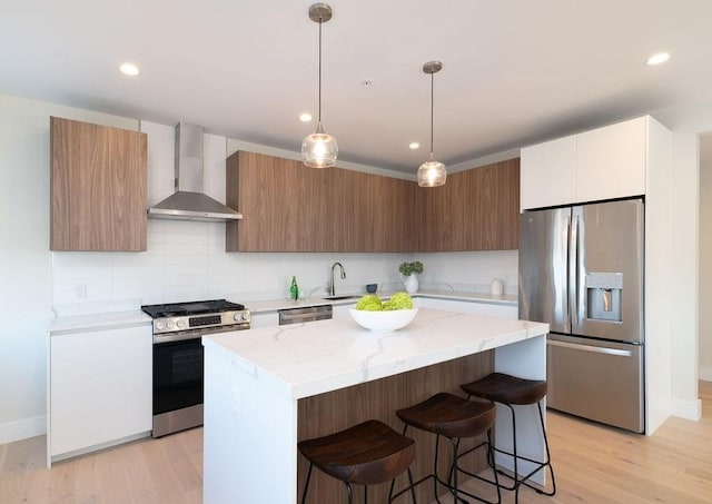 kitchen with light wood finished floors, a center island, stainless steel appliances, wall chimney range hood, and a kitchen bar