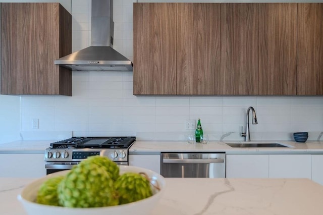 kitchen with wall chimney range hood, modern cabinets, stainless steel appliances, and a sink