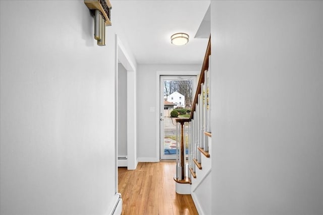 corridor with a baseboard heating unit, baseboards, stairway, and light wood-type flooring
