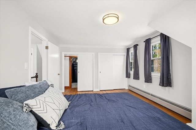 bedroom with multiple closets, wood finished floors, and a baseboard radiator