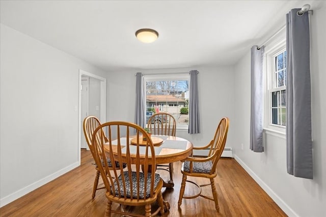 dining area with a baseboard radiator, light wood-type flooring, and baseboards