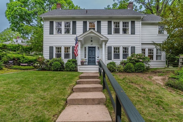colonial house with a chimney, a front lawn, and a shingled roof