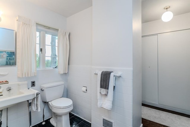 bathroom with toilet, wainscoting, tile patterned floors, and tile walls
