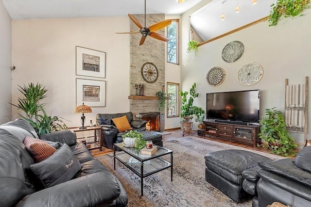 living room featuring a stone fireplace, a ceiling fan, high vaulted ceiling, and wood finished floors