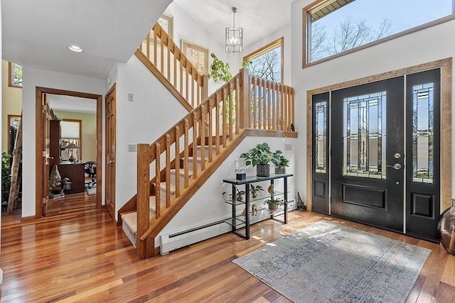 entrance foyer with a towering ceiling, recessed lighting, stairway, wood finished floors, and a baseboard radiator