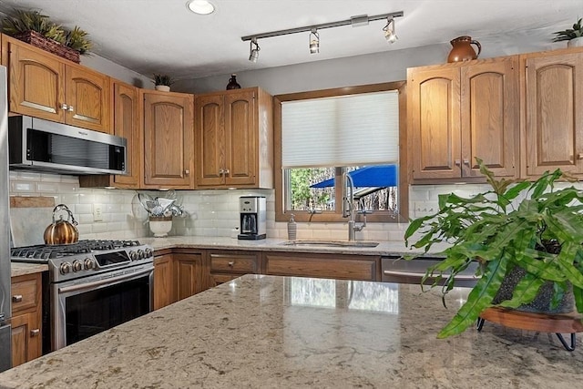 kitchen featuring stainless steel appliances, tasteful backsplash, a sink, and light stone counters