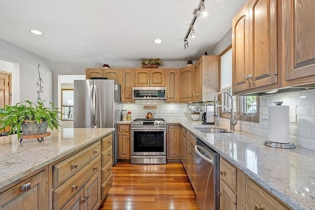 kitchen featuring tasteful backsplash, a sink, light wood-type flooring, appliances with stainless steel finishes, and light stone counters