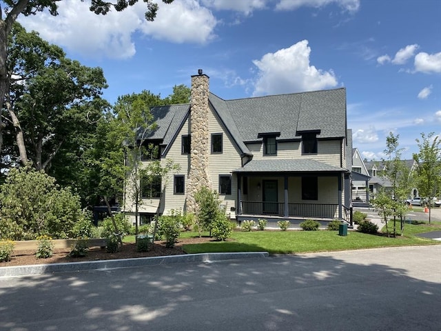 view of front of house featuring a front lawn, covered porch, a chimney, and a shingled roof