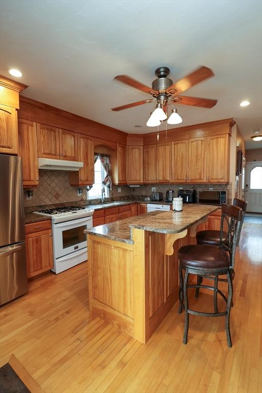 kitchen featuring tasteful backsplash, light wood-style flooring, freestanding refrigerator, under cabinet range hood, and white gas range oven