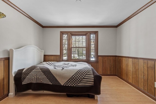 bedroom featuring crown molding, light wood-type flooring, wainscoting, and wood walls