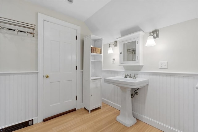 bathroom with a wainscoted wall, visible vents, vaulted ceiling, and wood finished floors