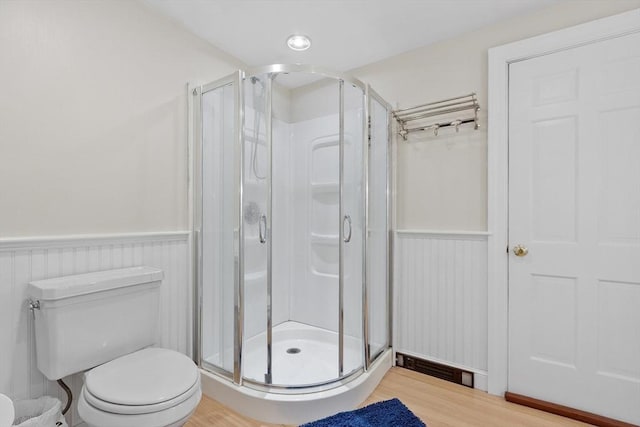 full bath featuring a wainscoted wall, wood finished floors, toilet, and a shower stall