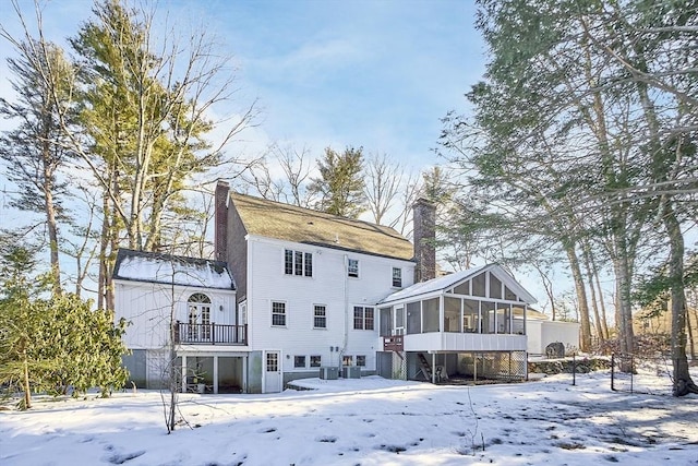 snow covered back of property with central air condition unit, a sunroom, and a chimney