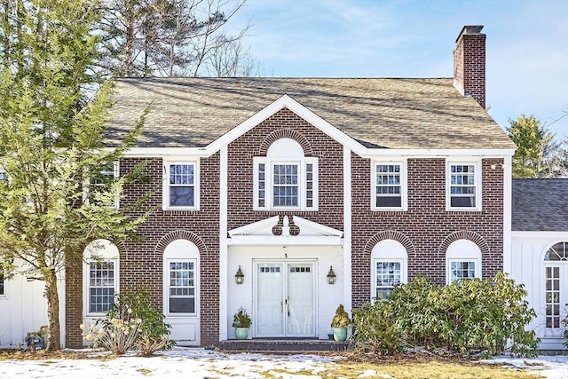 colonial-style house with brick siding, a chimney, and roof with shingles