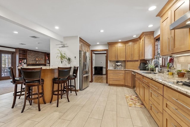 kitchen with stainless steel appliances, ventilation hood, a sink, and light stone countertops