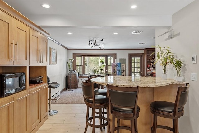 kitchen featuring black microwave, a peninsula, a breakfast bar, visible vents, and light stone countertops