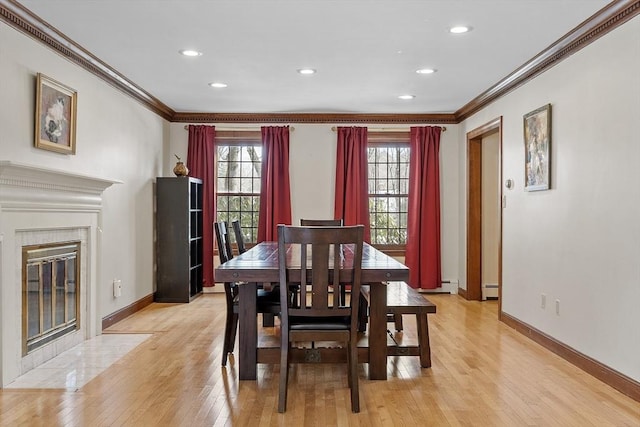 dining room with light wood finished floors, baseboards, crown molding, a baseboard heating unit, and a high end fireplace