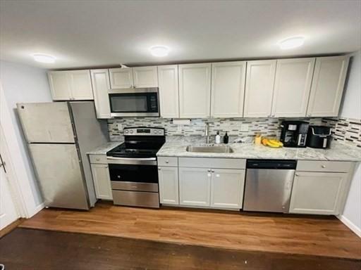 kitchen with appliances with stainless steel finishes, a sink, light countertops, decorative backsplash, and wood finished floors