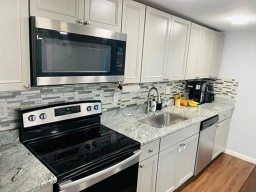 kitchen with tasteful backsplash, a sink, light wood finished floors, stainless steel appliances, and white cabinetry