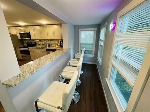 kitchen with dark wood-style flooring, light stone countertops, stainless steel appliances, baseboards, and tasteful backsplash
