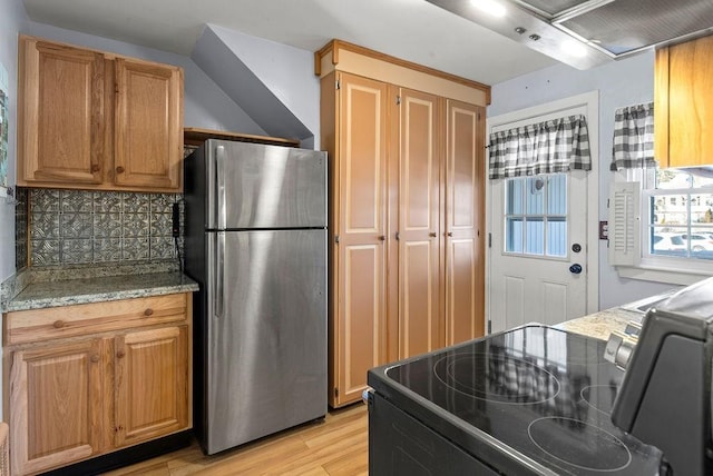 kitchen featuring range with electric stovetop, stainless steel fridge, decorative backsplash, light hardwood / wood-style floors, and light stone countertops