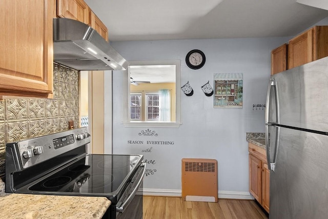 kitchen featuring extractor fan, backsplash, light stone counters, stainless steel appliances, and light hardwood / wood-style flooring