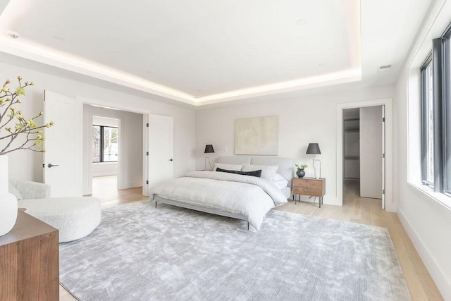 bedroom featuring baseboards, light wood-type flooring, a raised ceiling, and visible vents