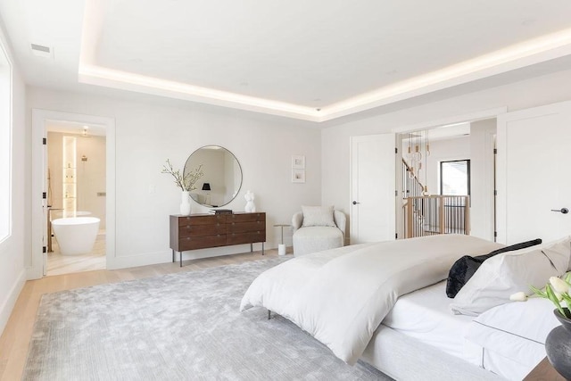 bedroom featuring light wood-type flooring, a tray ceiling, baseboards, and visible vents