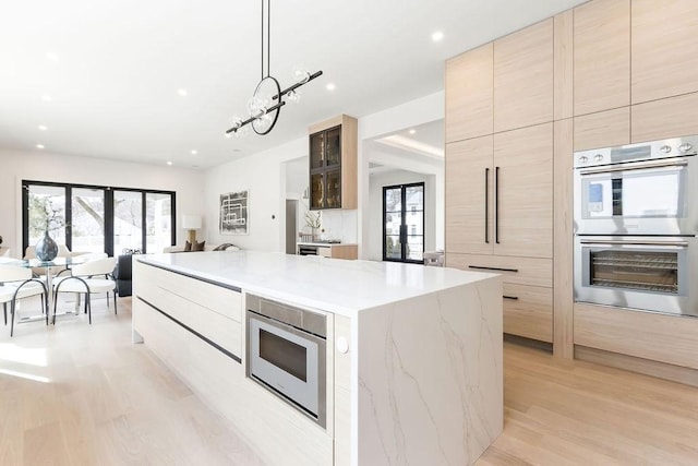 kitchen with a spacious island, light brown cabinets, light wood-style floors, stainless steel appliances, and modern cabinets