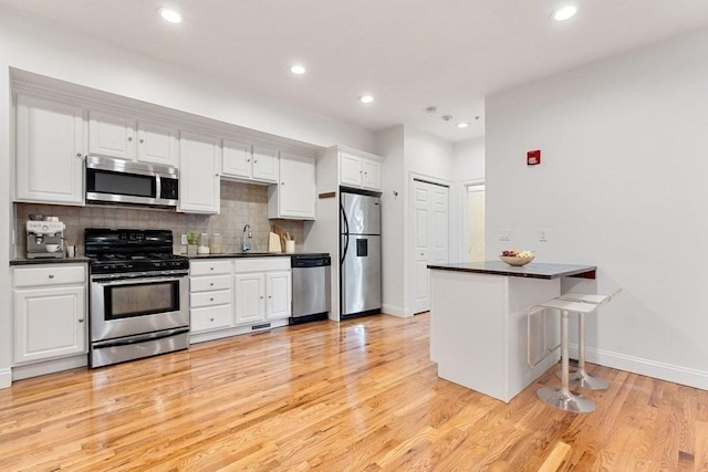 kitchen featuring dark countertops, white cabinetry, a sink, appliances with stainless steel finishes, and backsplash